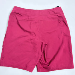 A pair of women's athletic shorts in a dusty rose pink color, laid flat on a white surface with the tips of light-colored sneakers visible at the bottom edge.