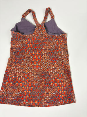 A sleeveless halter-style dress with a dense geometric and tribal-inspired pattern in orange, red, brown, and blue, featuring a solid purple lining visible at the neckline.
