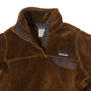 A brown fleece quarter-zip pullover jacket by Patagonia, featuring a stand-up collar, dark gray snap-button placket, and a small Patagonia logo patch on the left chest.